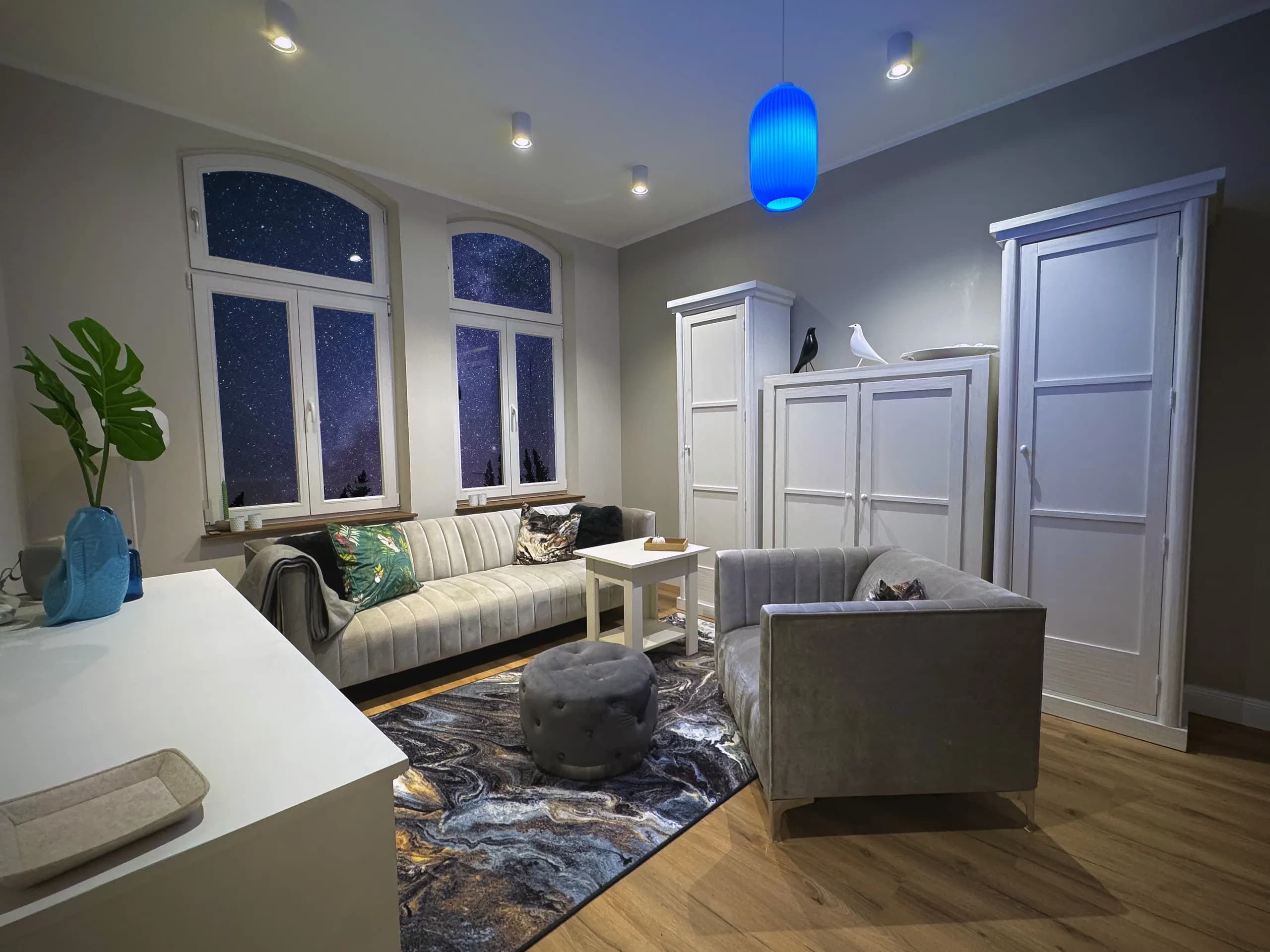 Wohnzimmer der Wohnung Vios mit grauem Sofa und Rundbogenfenstern, möbliertes Apartment in Bad Oeynhausen.